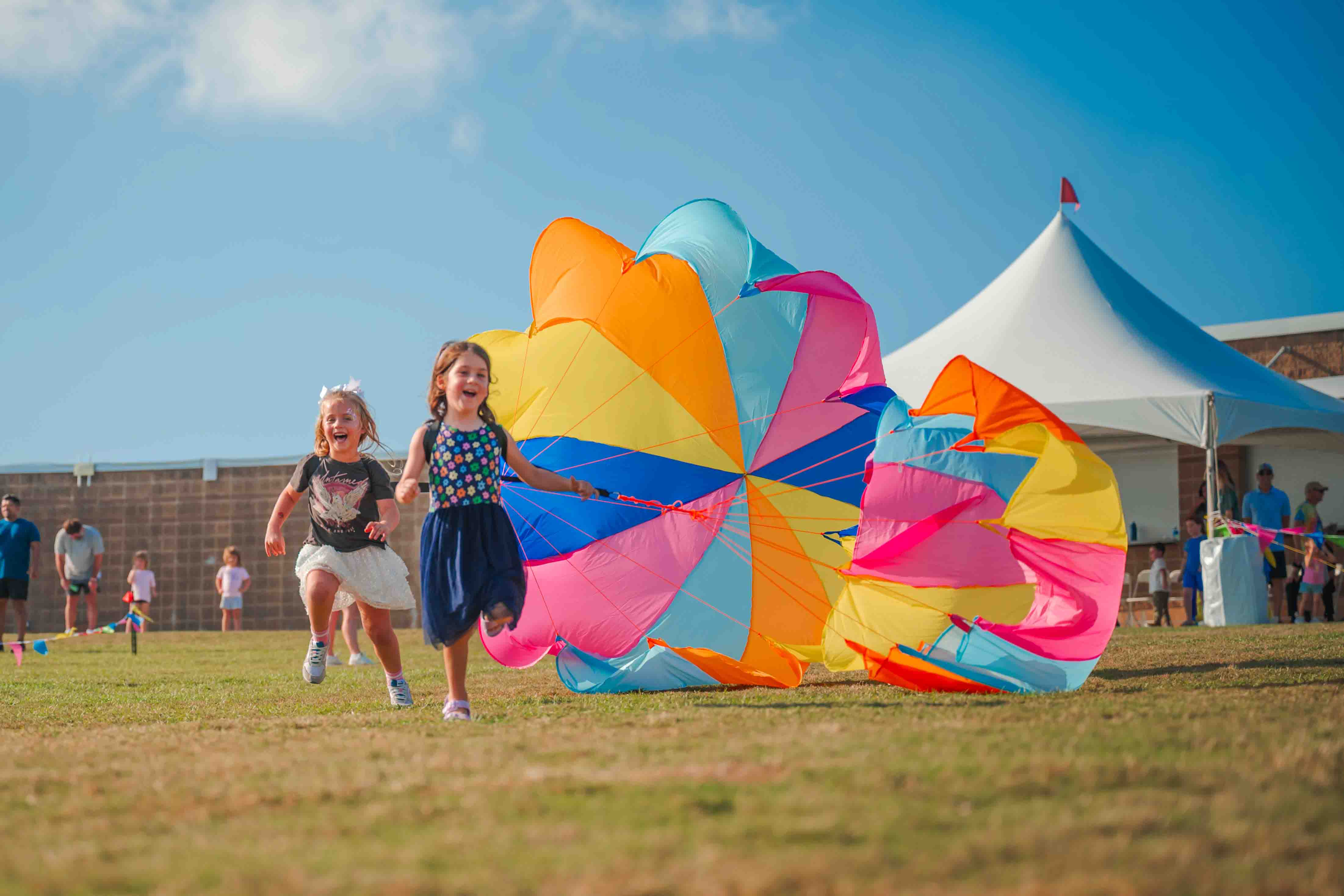 Children run on the lawn with bright, wind-filled parachutes.