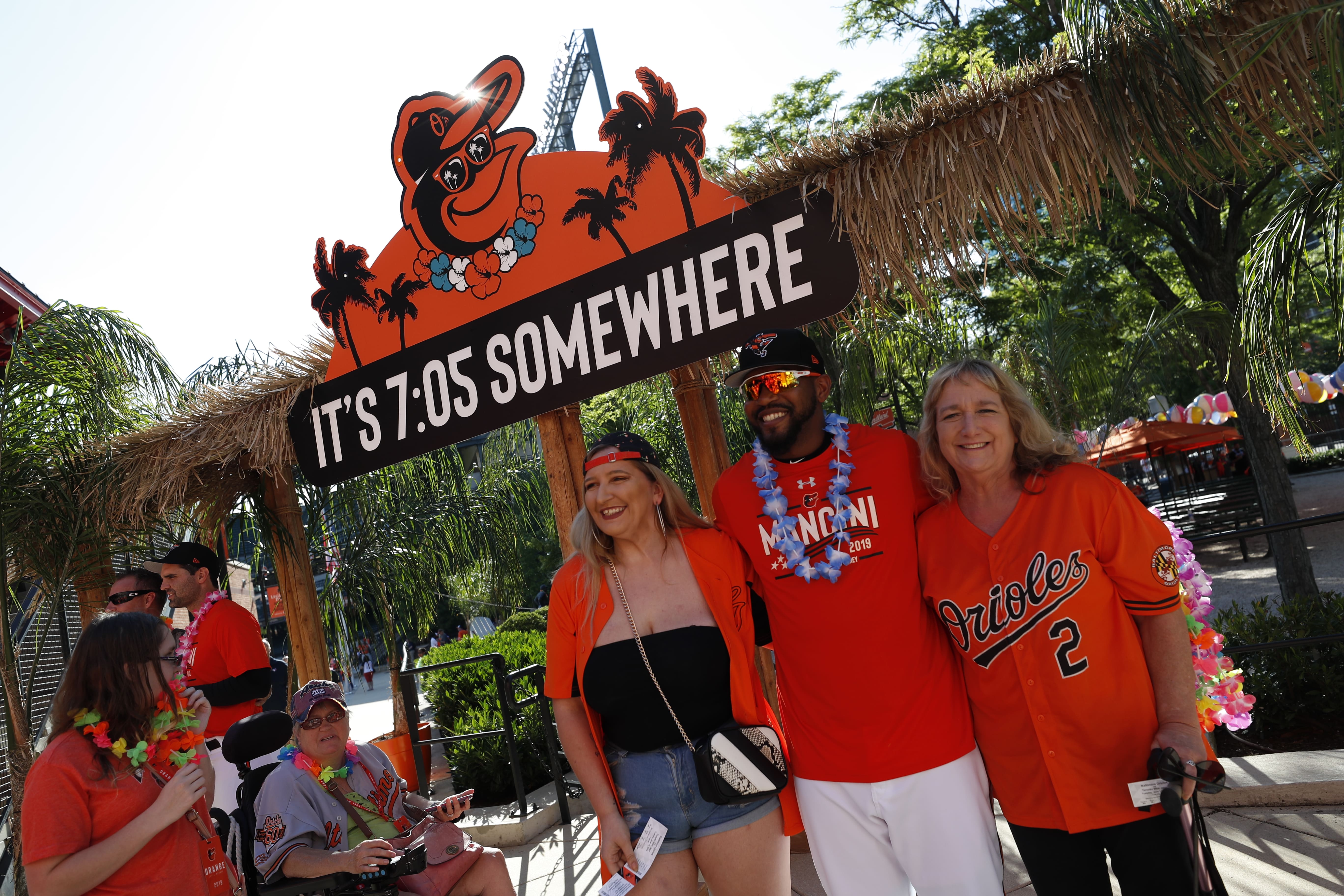 Baltimore Orioles fans posing at a themed photo op featuring a IT'S 7:05 SOMEWHERE sign