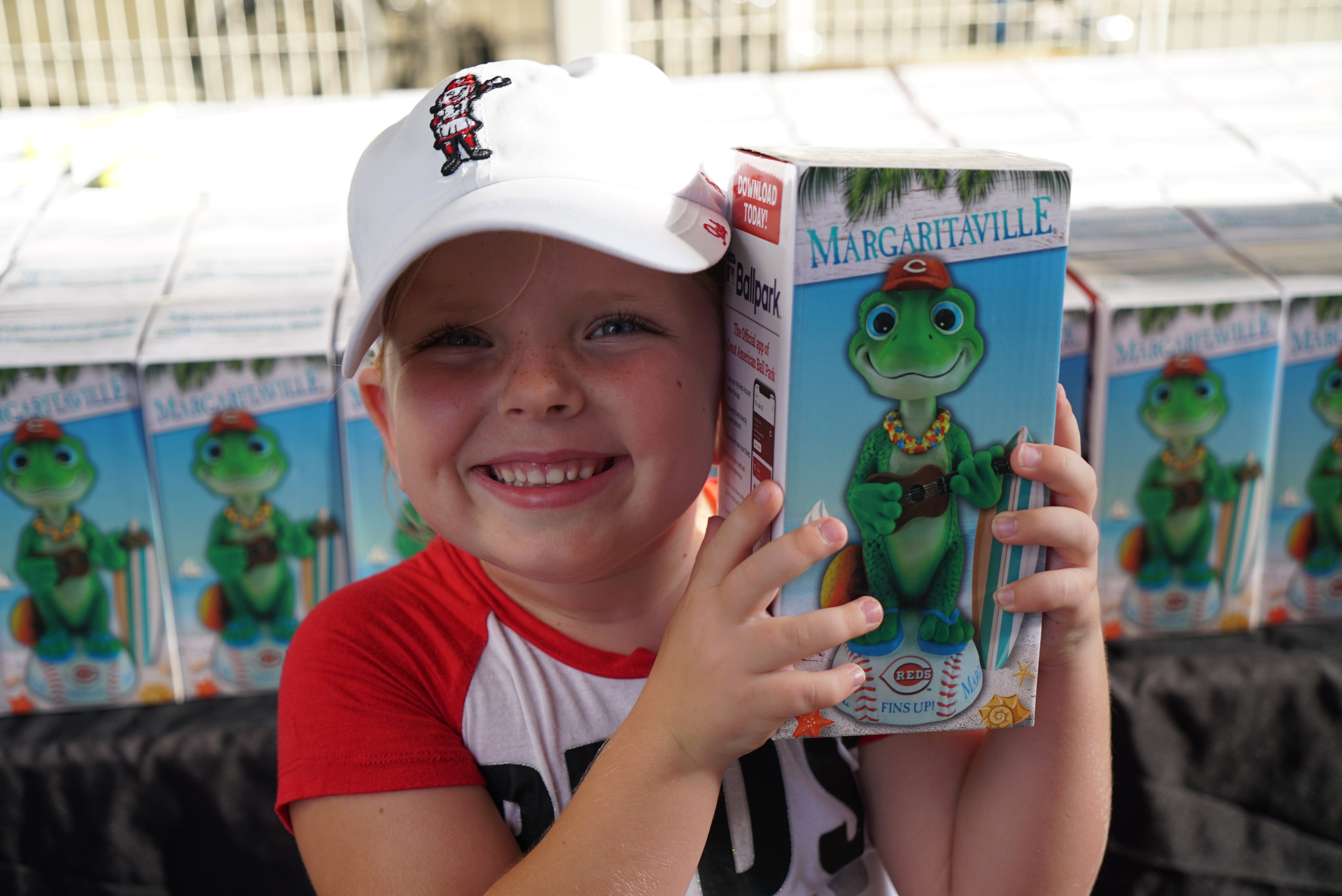 A young fan smiling and holding a Margaritaville bobblehead box at a Cincinnati Reds game