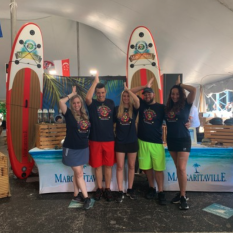 A group of five people in matching promotional t-shirts posing at a Margaritaville event