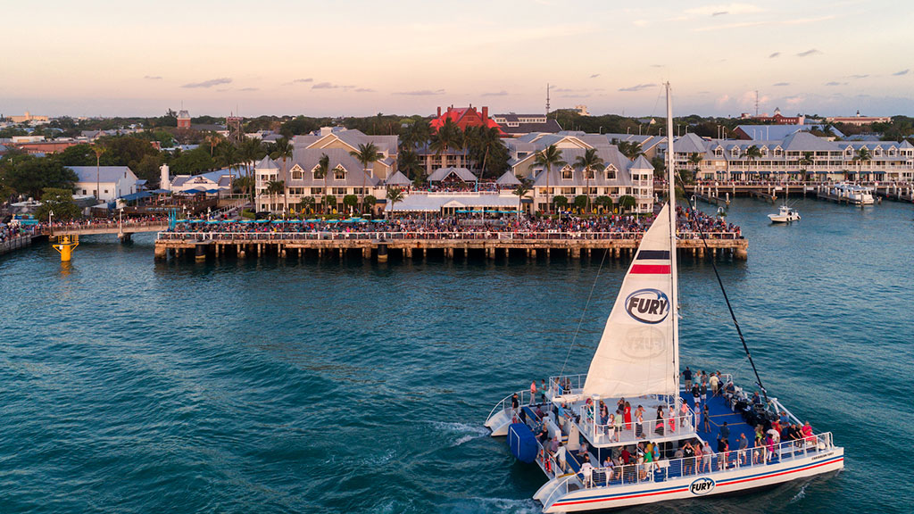 A resort with a lot of people on the pier and a pleasure boat